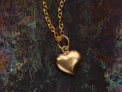 thumbnail of Reverse side of a gold heart-shaped pendant necklace on dark colorful background.

