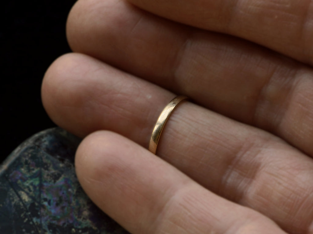 Narrow slightly rounded 10k yellow gold band, shown on white background. Shown on finger.