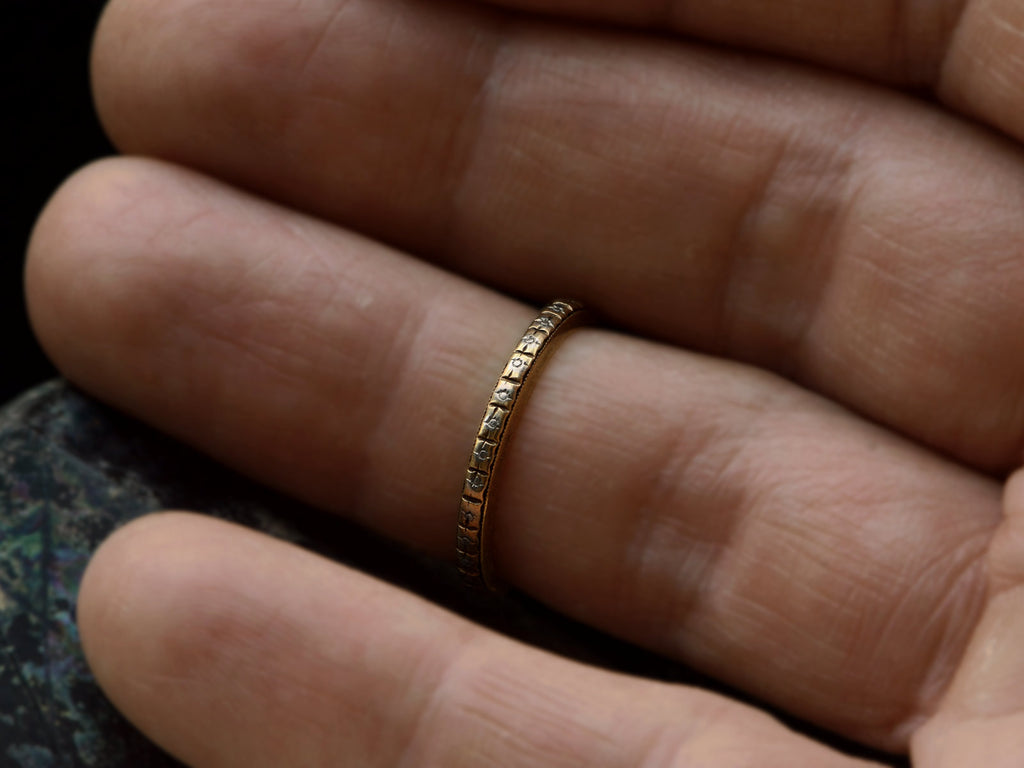 A c1920 thin yellow gold Art Deco wedding band with patterning and white gold accents, shown worn on finger.