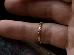 thumbnail of A narrow vintage rosy-yellow wedding band with a pattern of flowers and facets, shown on a hand