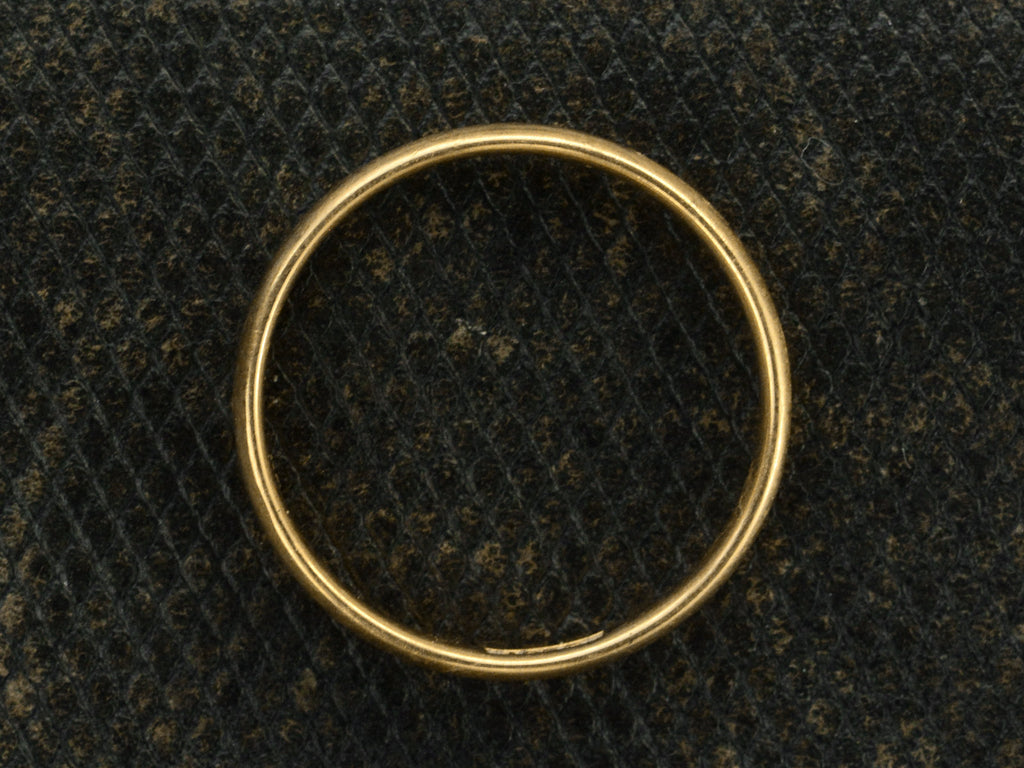 Side profile of an antique rounded 18K yellow gold wedding band, shown on dark textured background.