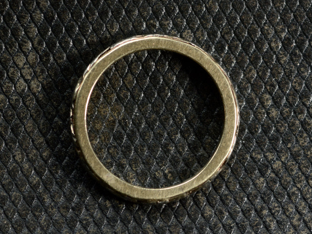 Side profile of a yellow c1920 Art Deco wedding band with white gold decoration on the outside face, shown on dark textured background.
