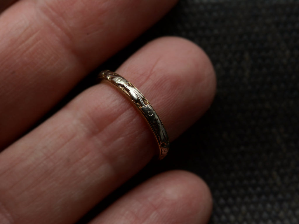 A yellow c1920 Art Deco wedding band with white gold decoration on the outside face, shown on finger