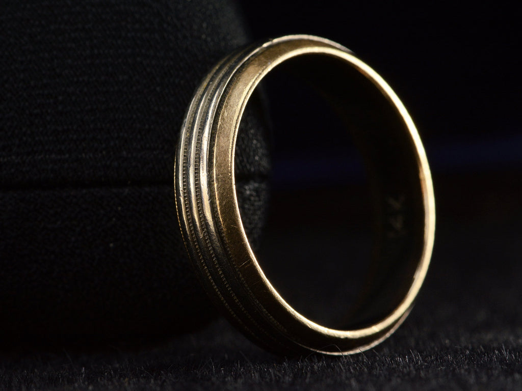 Angled side view of vintage men's wedding band in yellow gold with center stripes of white gold, shown on dark background