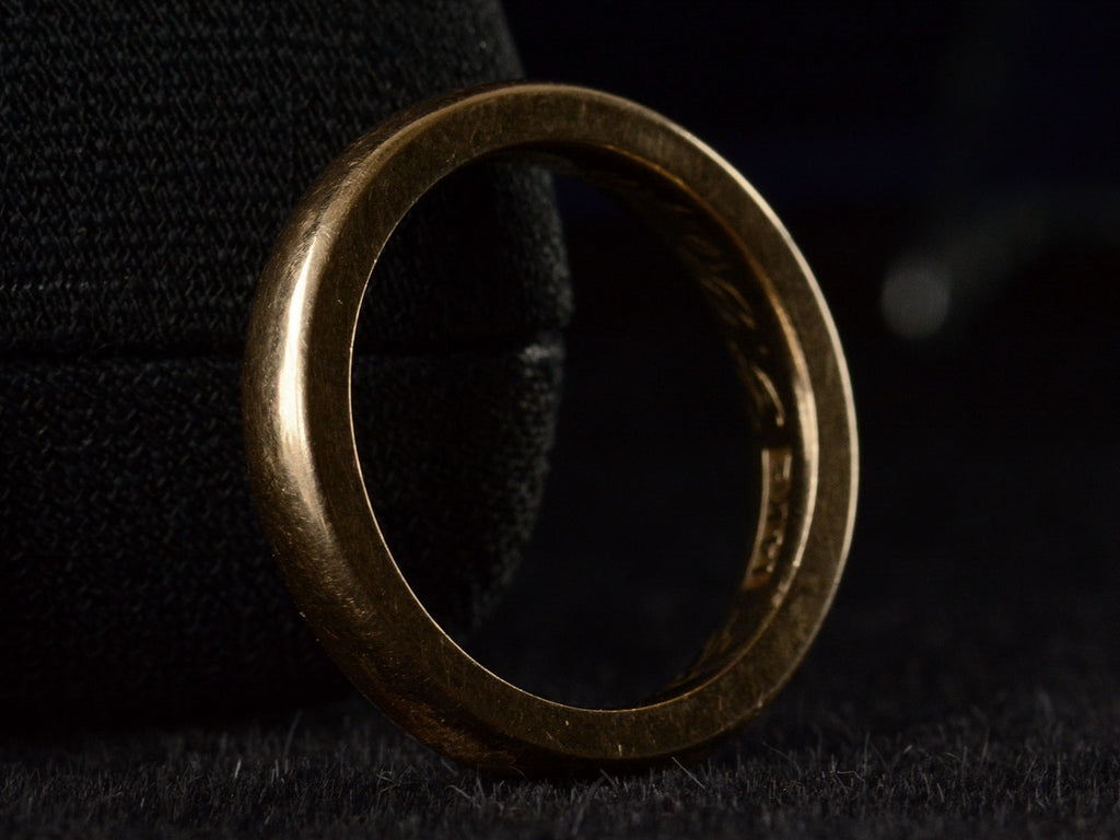 Angled side view of a heavy antique wedding band in a rosy-yellow gold measuring 3.2mm wide. Shown on dark background. A "14K" stamp is visible inside as well as an indecipherable inscription.