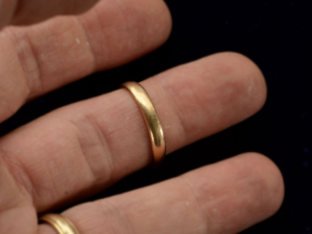 A patinated 14k yellow gold men's wedding band with a slightly rounded profile, shown on a finger