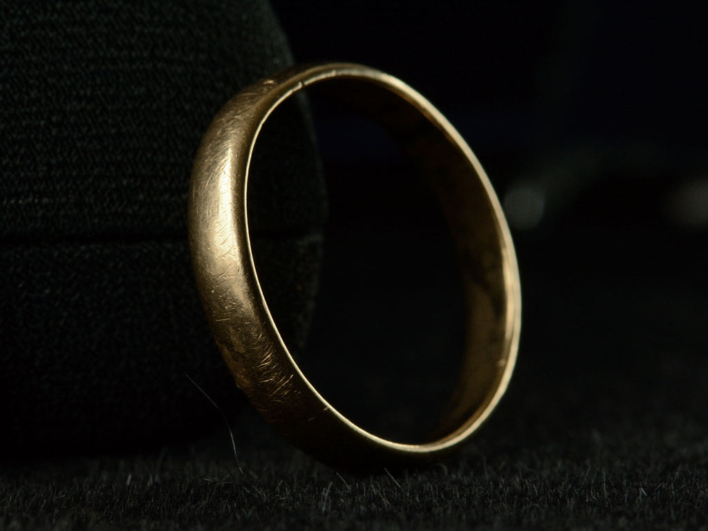 Angled view of a patinated 14k yellow gold men's wedding band with a slightly rounded profile, shown on dark background.