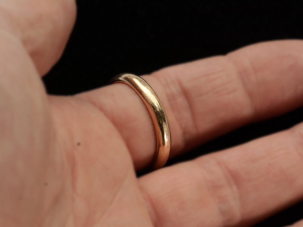 An antique rounded rosy-yellow 14k gold wedding band, shown on finger.