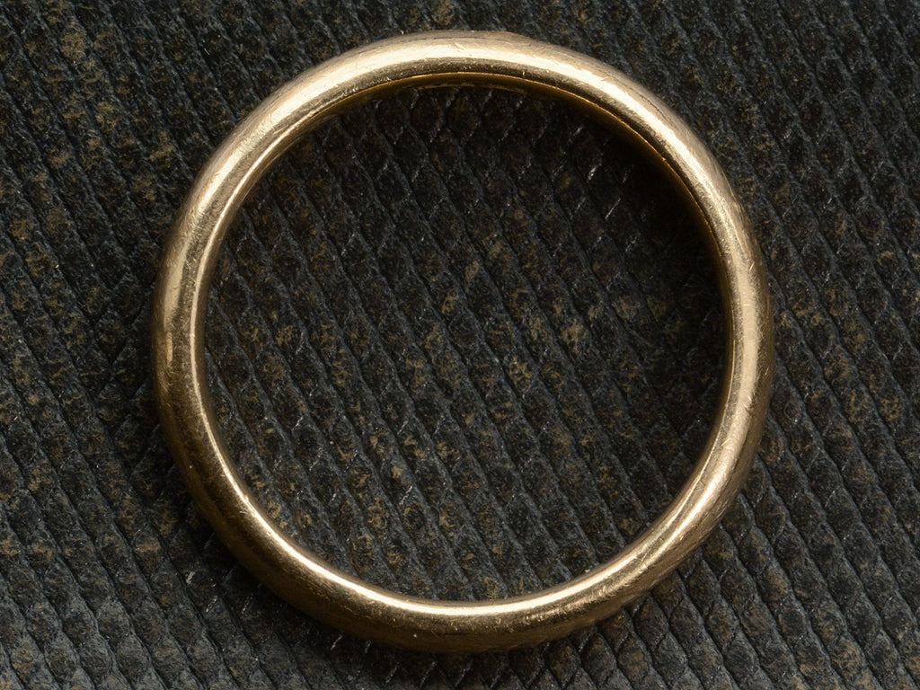 Side profile view of an antique rounded rosy-yellow 14k gold wedding band, shown on textured dark background.
