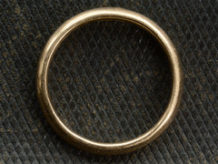 thumbnail of Side profile view of an antique rounded rosy-yellow 14k gold wedding band, shown on textured dark background.