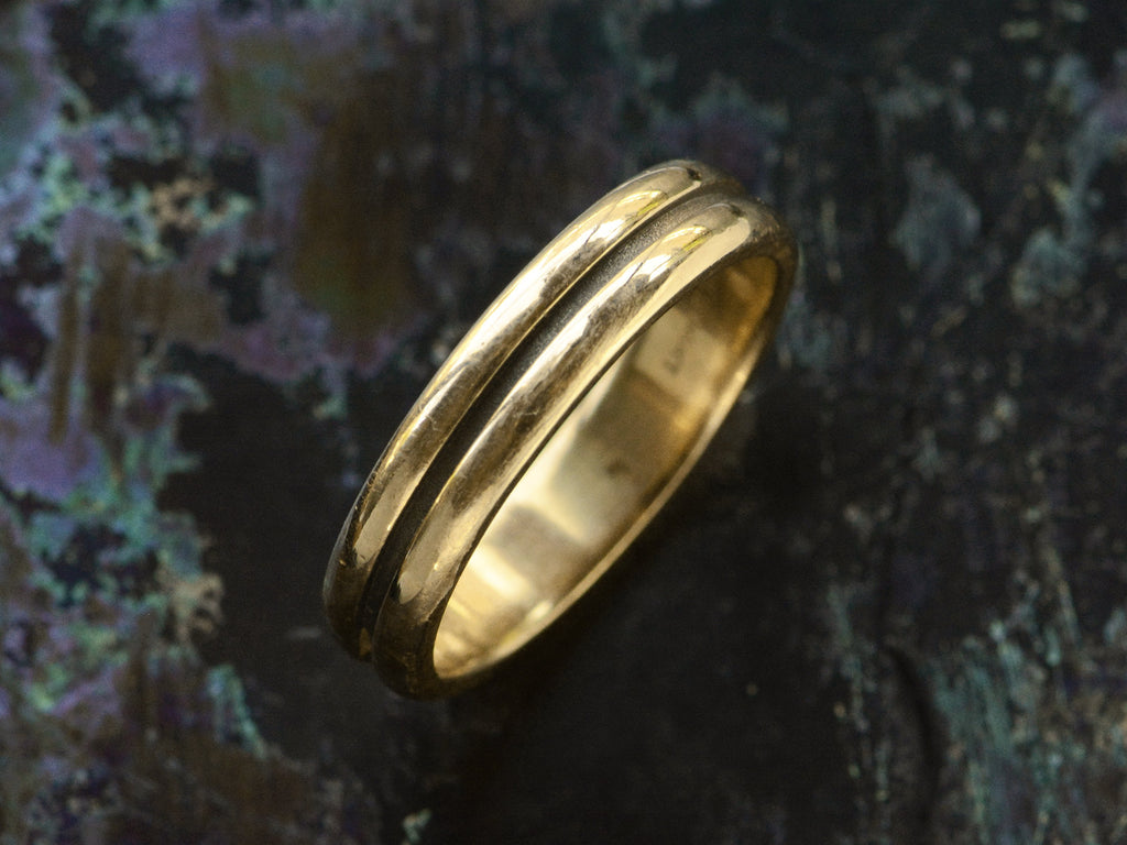 Angled view of medium width vintage 14k yellow gold wedding band with a groove cut down the middle, shown on dark background.