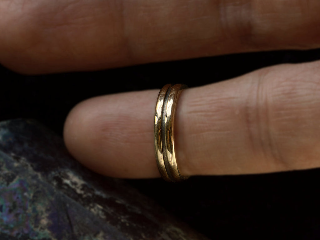 A medium width vintage 14k yellow gold wedding band with a groove cut down the middle, shown on finger