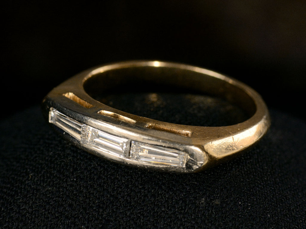 Elevated angled view of two toned vintage ring with three diamond baguettes. Shown on dark background.