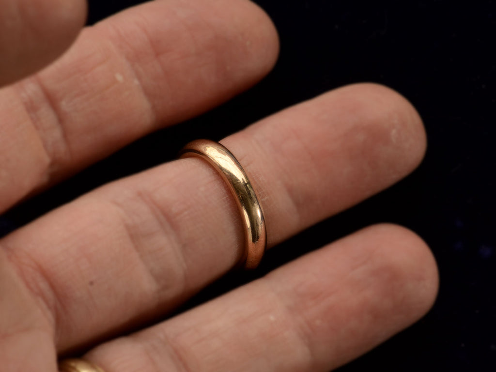 A rounded 4.0mm wide antique rosy-yellow gold wedding band, shown on finger.