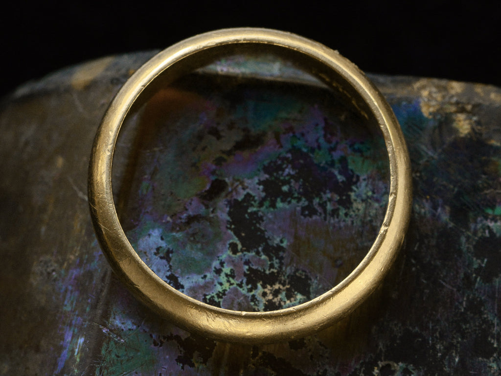 Side profile of vintage men's 14K yellow gold wedding band with rounded surface and patina, shown on dark iridescent background.