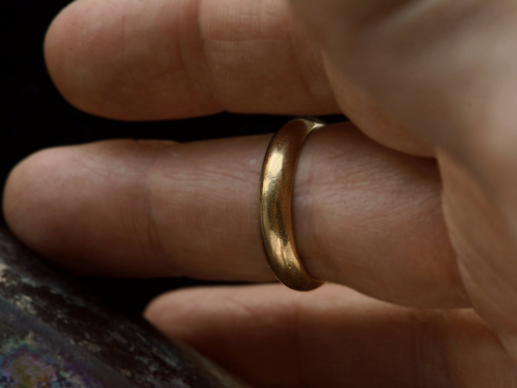 Vintage men's 14K yellow gold wedding band with rounded surface and patina, shown on finger