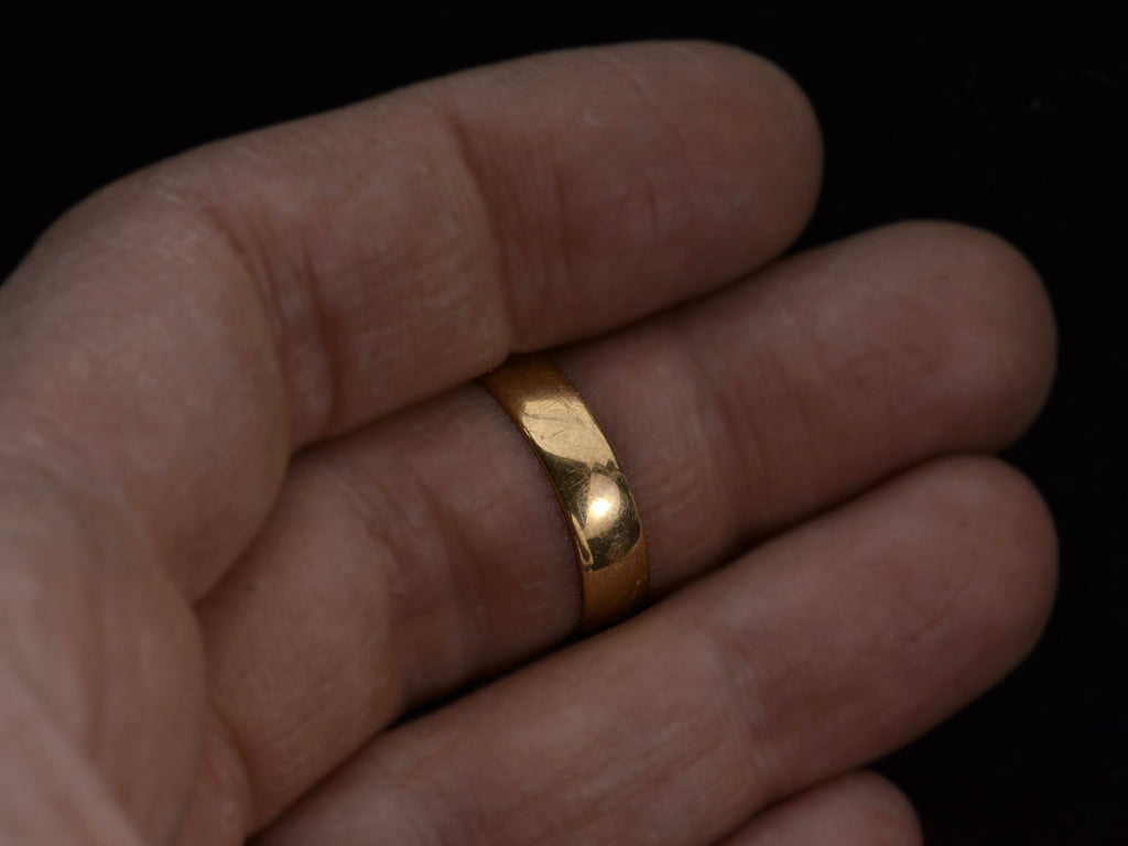 Wide flat 18K yellow gold antique wedding band, on finger.