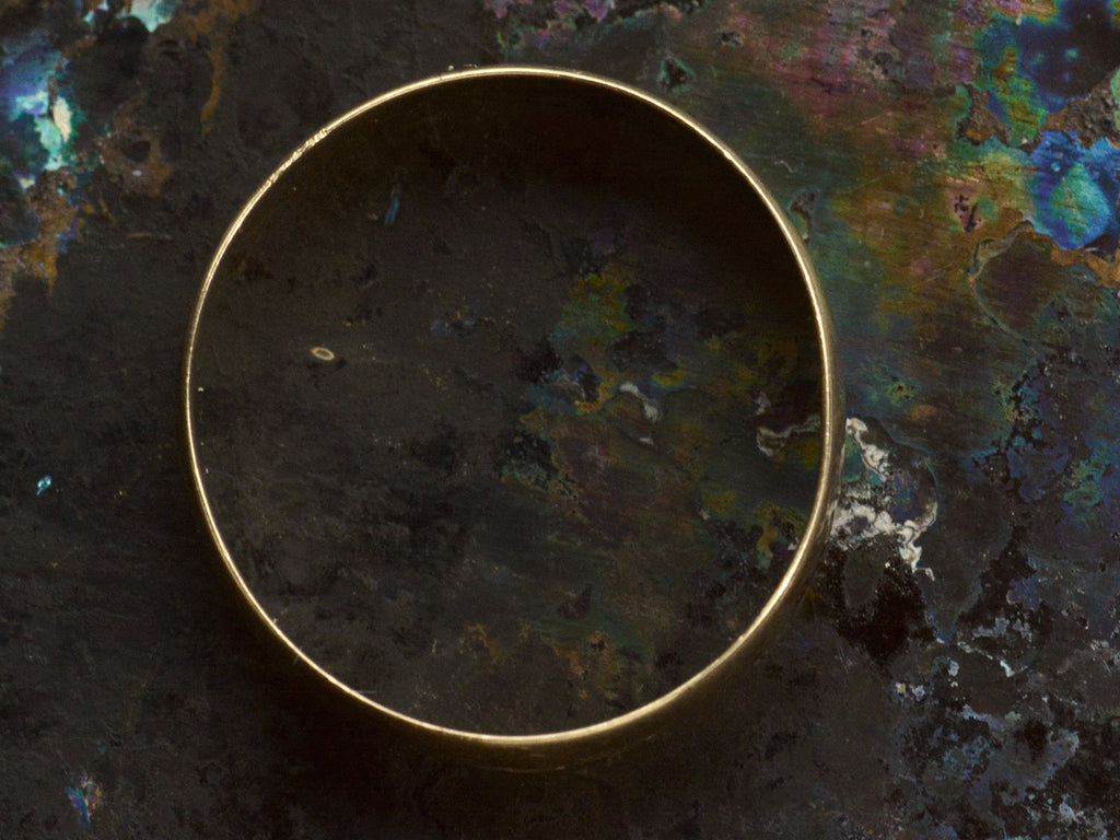 Side profile of wide flat 18K yellow gold antique wedding band, on dark background.