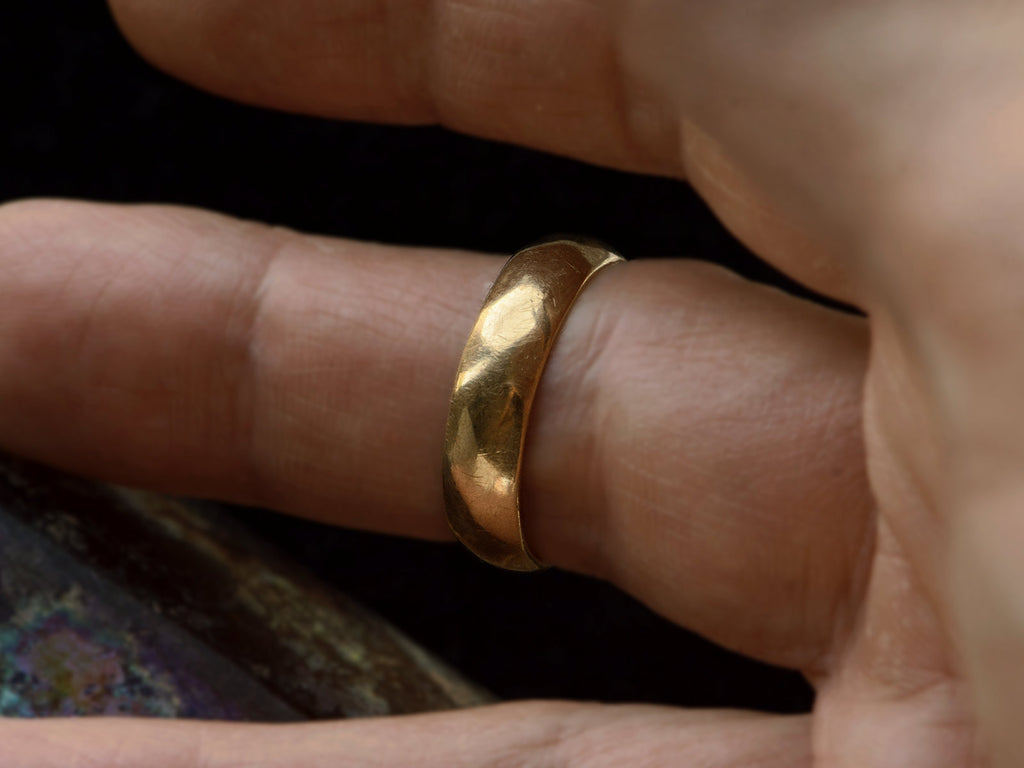 A 5.5mm wide vintage men's wedding band with a modeled surface, shown on finger. 