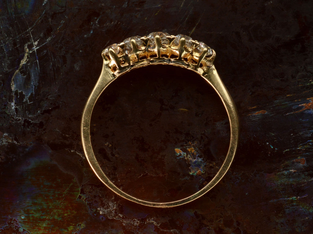 Side profile of antique c1900 ring with five small diamonds set in a row in 18K yellow gold. Shown on dark background.