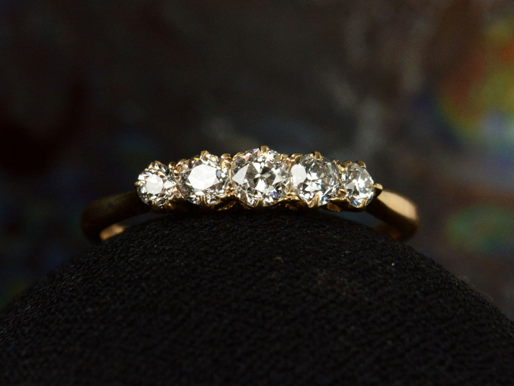 Front of antique c1900 ring with five small diamonds set in a row in 18K yellow gold. Shown on dark background.