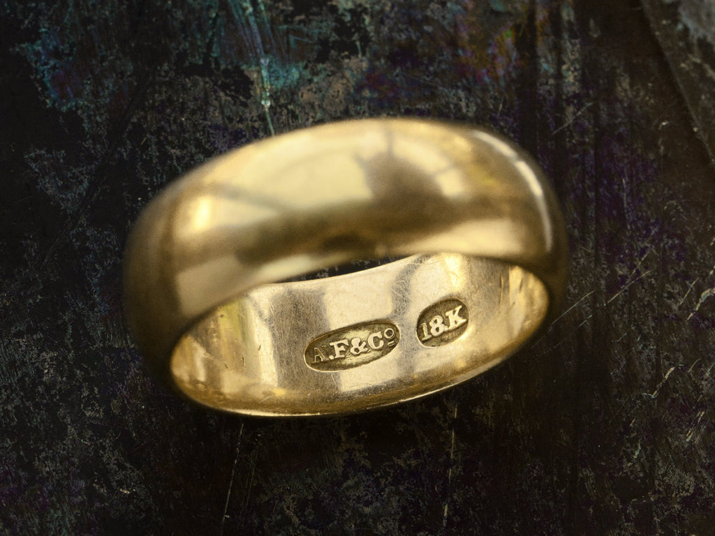 Detail of stamps inside a wide antique 18K yellow gold wedding band on dark background. Stamps read "A.F.&Co." and "18K"