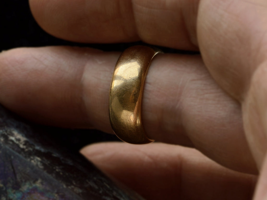 A wide antique 18K yellow gold wedding band with patinated surface, shown on finger.
