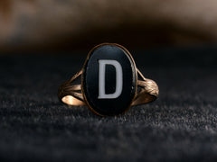 thumbnail of Front of c1890 Victorian signet ring with oval black plaque and white letter "D". Set in brass and shown on dark background.