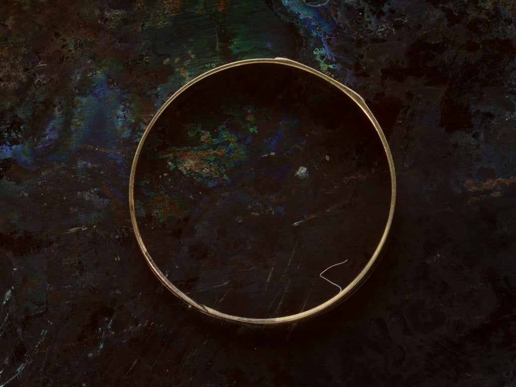 Side profile of a petite antique gold signet ring with the letters "I.N" engraved on a rectangular face. Shown on dark background.