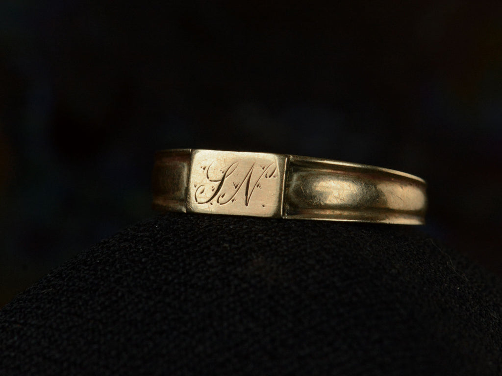 Right front angled view of a petite antique gold signet ring with the letters "I.N" engraved on a rectangular face. Shown on dark background.