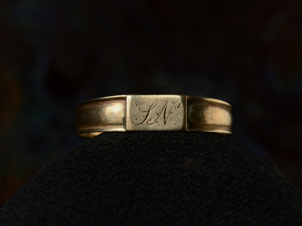 Front view of a petite antique gold signet ring with the letters "I.N" engraved on a rectangular face. Shown on dark background.