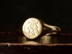 thumbnail of Angled view of an antique 18K gold signet ring with a monogram (letters A and J) engraved on the face. Shown on dark background.
