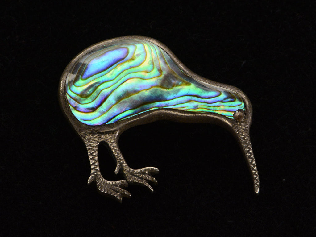 A kiwi bird brooch with iridescent abalone shell set in silver, shown on black background.