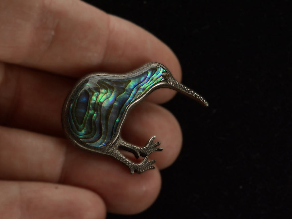 A kiwi bird brooch with iridescent abalone shell set in silver, shown held in hand