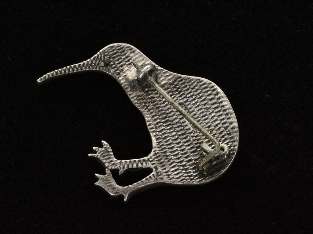 Reverse side of kiwi bird brooch with textured surface, shown on black background.