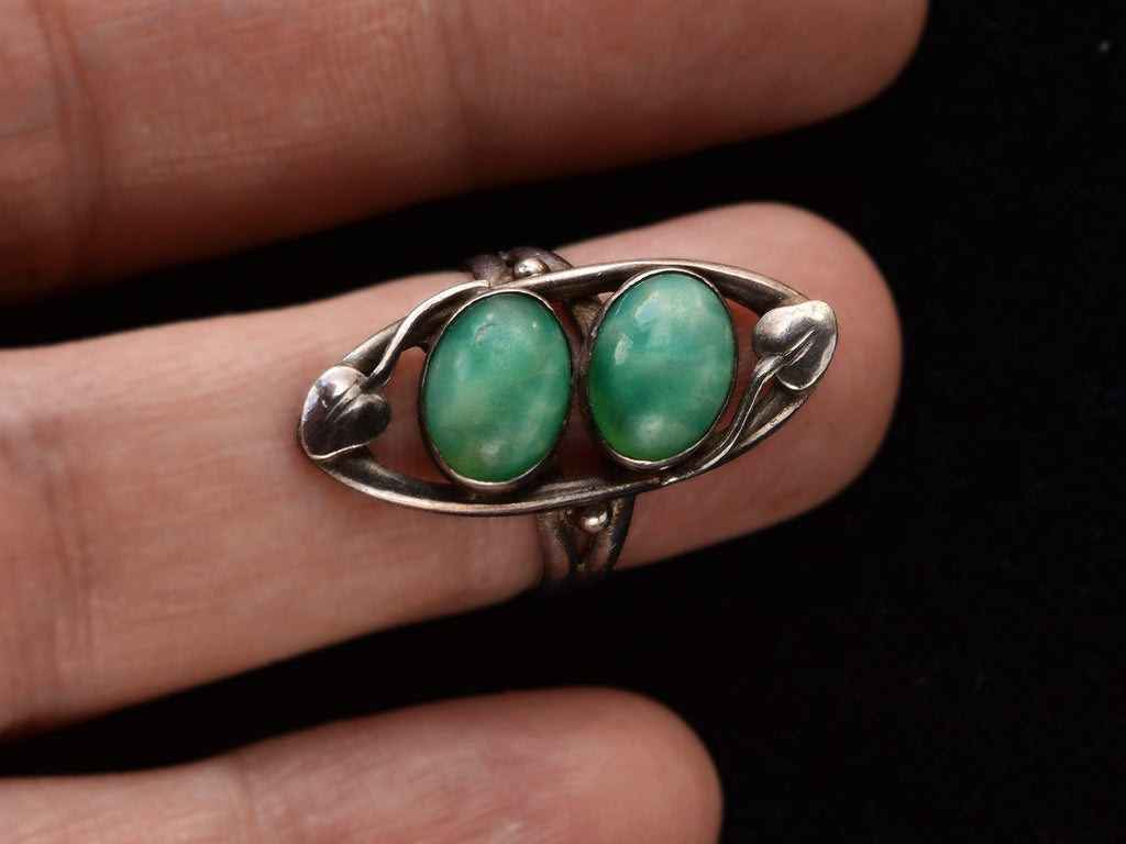 c1910 Arts & Crafts movement ring with a pair of oval green stones in a silver mounting with vines. On finger.
