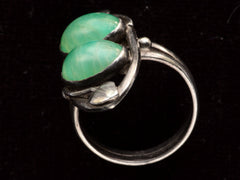 thumbnail of Side profile of c1910 Arts & Crafts movement ring with a pair of oval green stones in a silver mounting with vines. On black background.