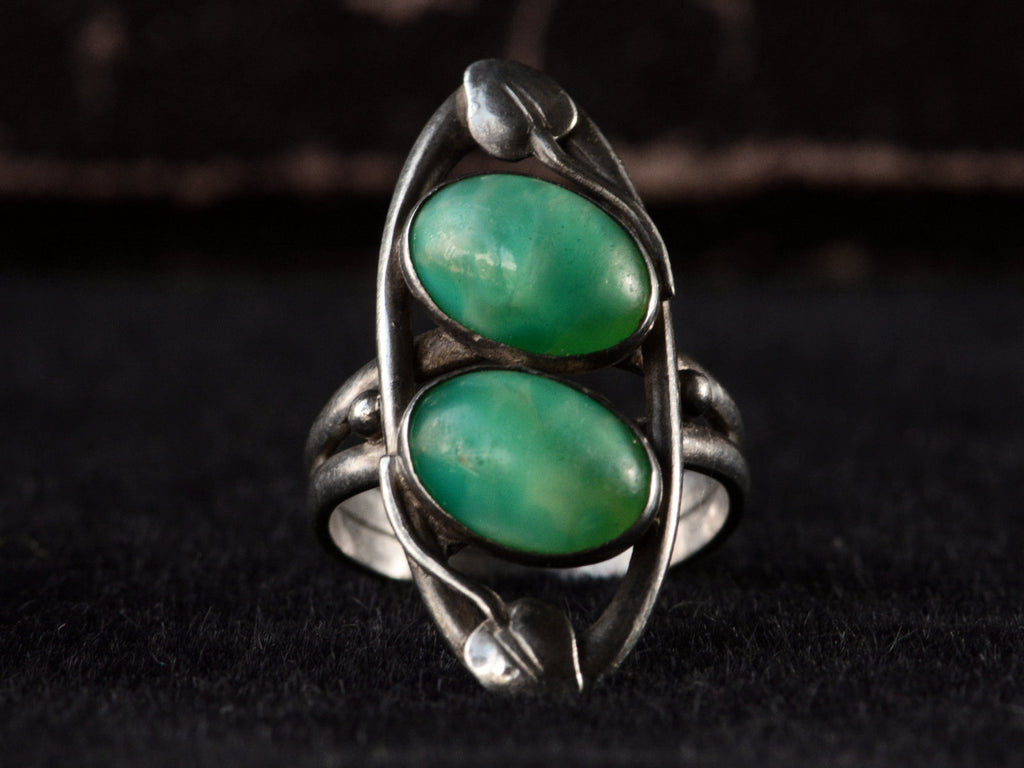 Front view of c1910 Arts & Crafts movement ring with a pair of oval green stones in a silver mounting with vines. On black background.