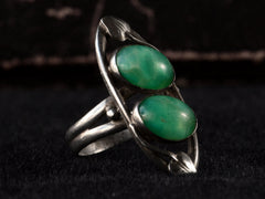 thumbnail of Left angled view of c1910 Arts & Crafts movement ring with a pair of oval green stones in a silver mounting with vines. On black background.