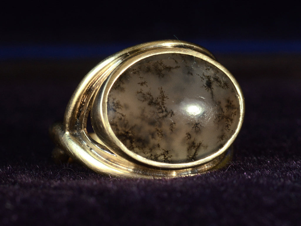 Angled front of oval dendritic agate ring in yellow gold. Shown on dark background.