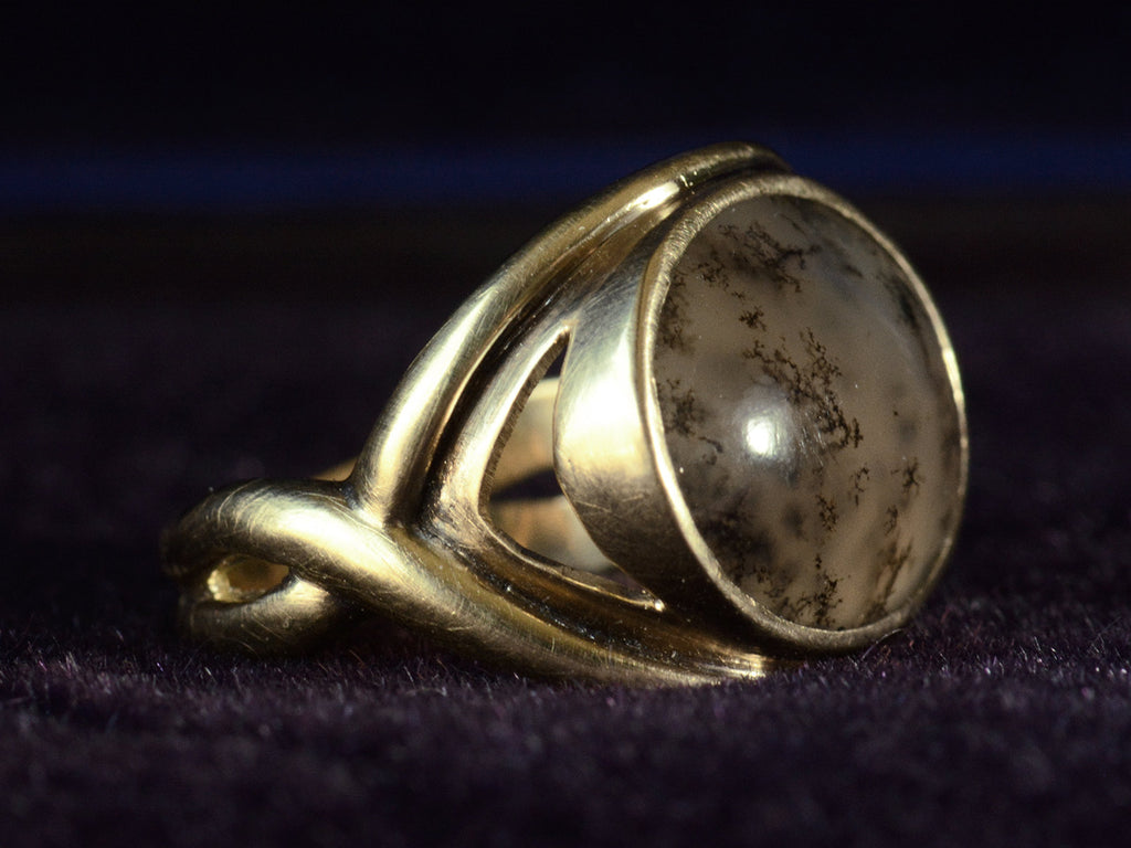 Side view of oval dendritic agate ring in yellow gold. Shown on dark background.