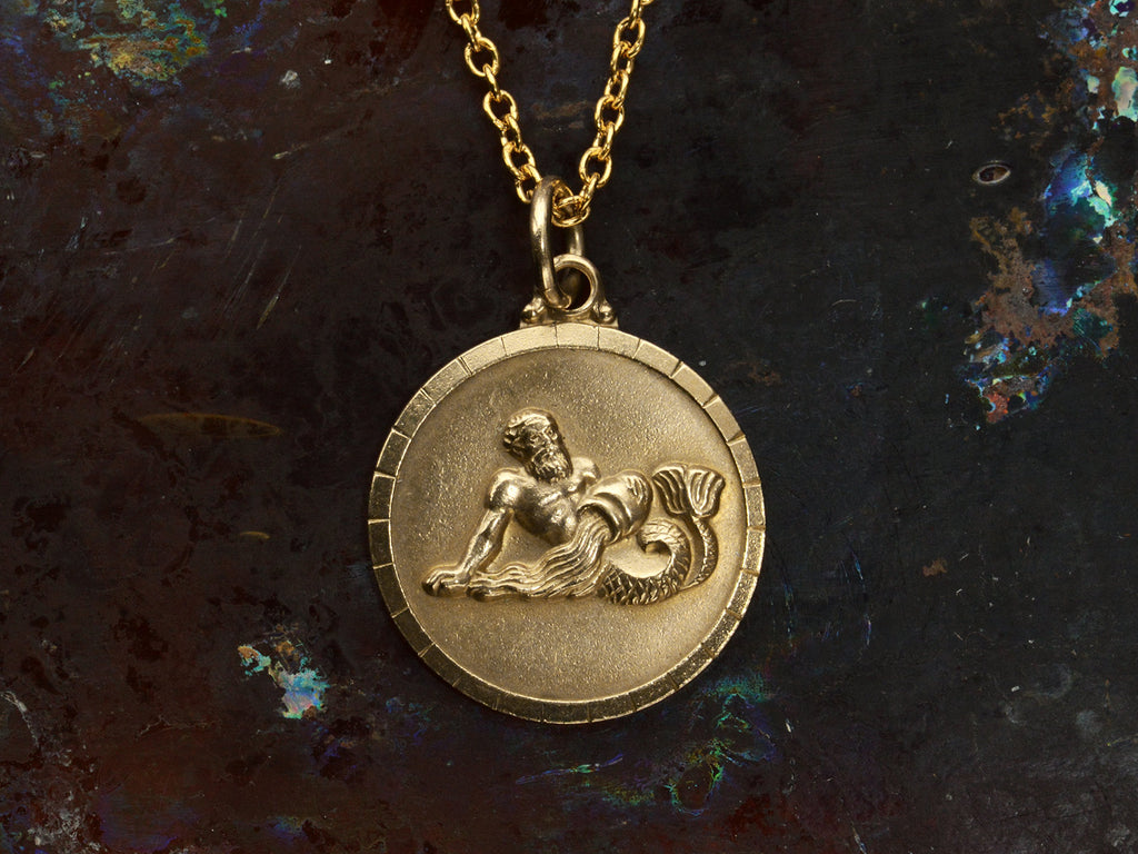 Vintage round gold pendant depicting the water bearer, symbolism for Aquarius. Shown on dark background.