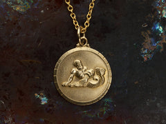 thumbnail of Vintage round gold pendant depicting the water bearer, symbolism for Aquarius. Shown on dark background.