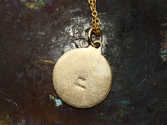thumbnail of Reverse side of vintage round gold pendant, stamped with tiny illegible English hallmarks. Shown on dark background.