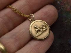 thumbnail of Vintage round gold pendant depicting the water bearer, symbolism for Aquarius. Shown on hand.