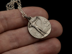 thumbnail of A vintage white metal archery medal with an archer pictured in relief. Shown held in hand.