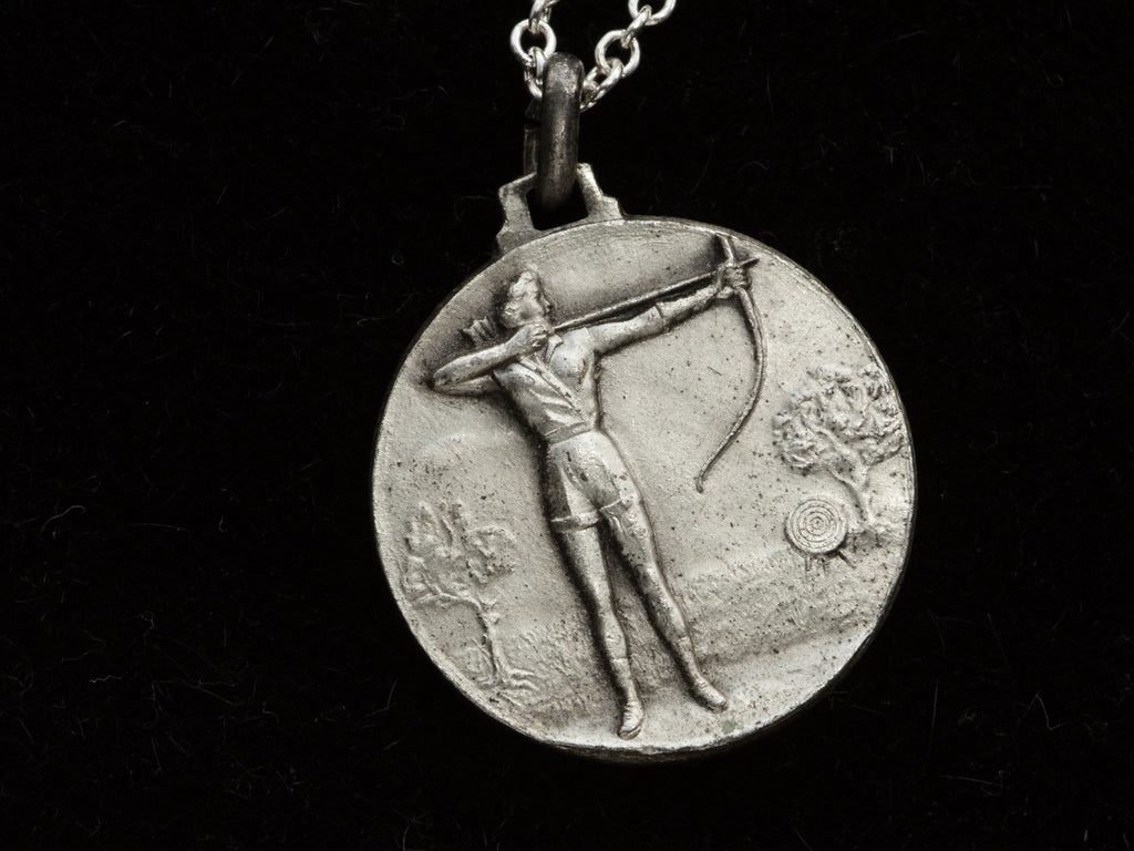 Detail of a vintage white metal archery medal with an archer pictured in relief. Shown on black background.
