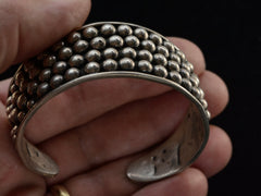 thumbnail of A close-up of a hand holding a wide vintage silver cuff bracelet decorated with rows of small metallic beads, set against a dark background.