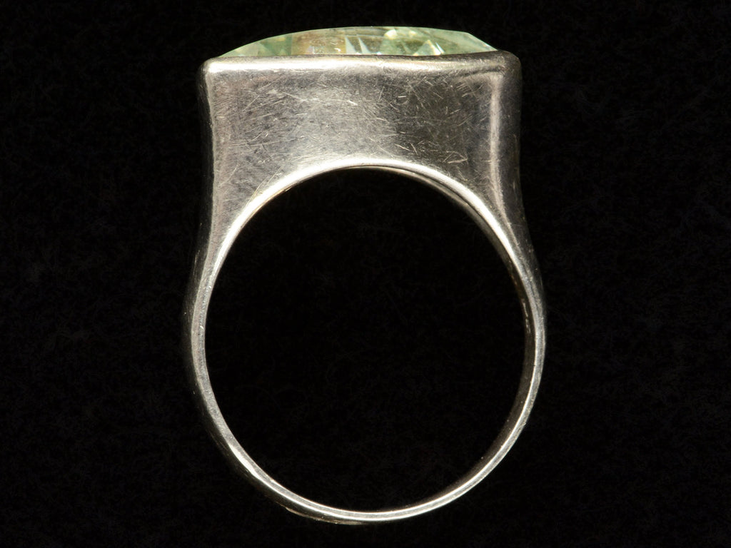 Side profile view of silver ring with faceted light green eye-shaped stone, shown on dark background.