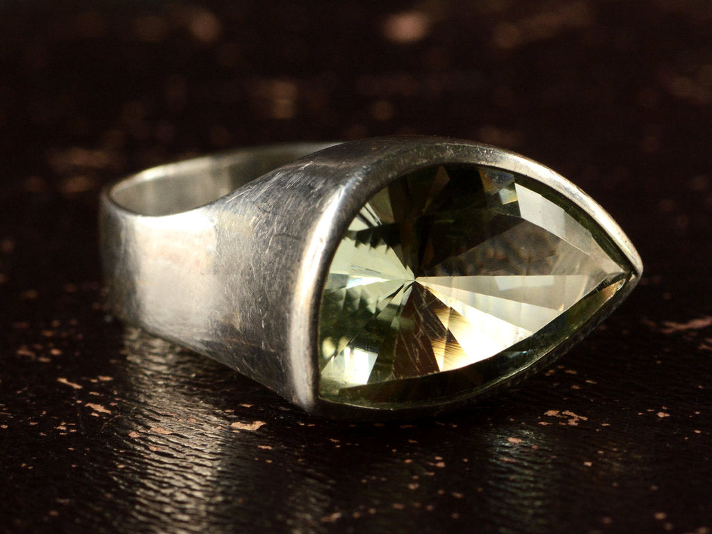 Right angled view of silver ring with faceted light green eye-shaped stone, shown on dark background.